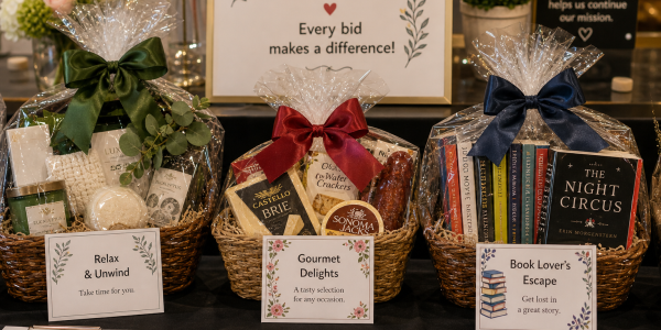 Wrapped gift baskets with ribbon and printed bid sheets displayed on a charity auction table