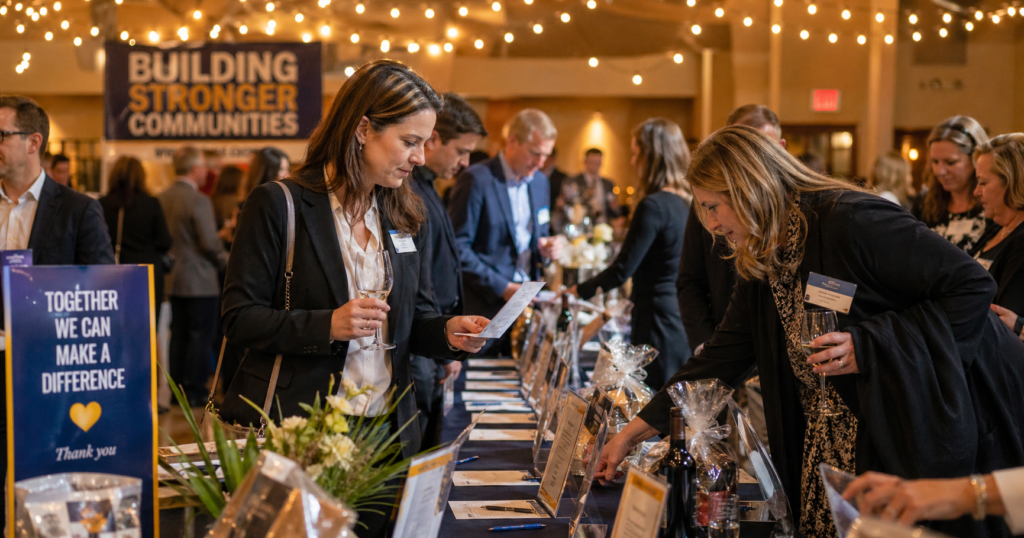 Guests mingling and bidding at a silent auction fundraiser event, illustrating effective silent auction promotion driving attendance