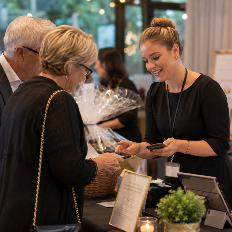 Volunteer helping guests during silent auction checkout at nonprofit fundraiser
